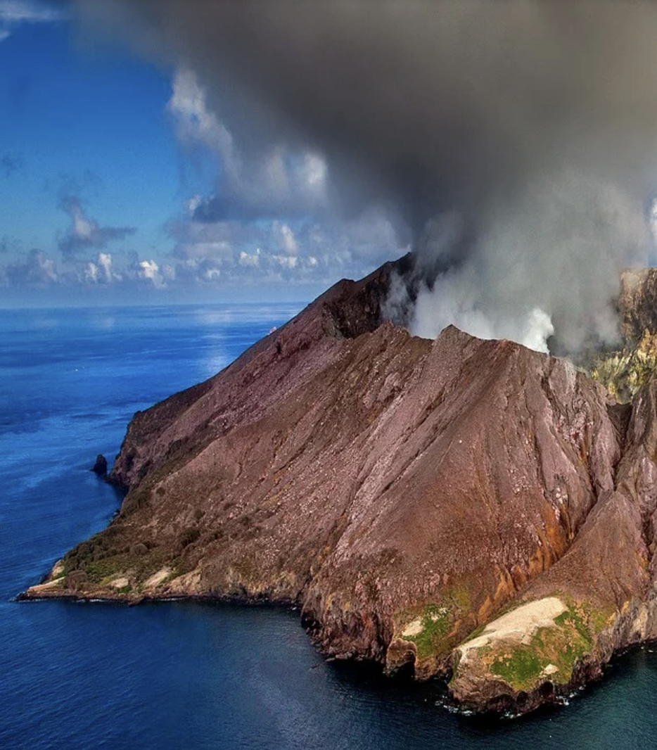 mountain with smoke out of the top surrounded by an ocean